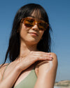 Woman applying sunscreen lotion to shoulder with blue sky background