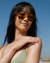 Woman applying COOLA hydrating sunscreen lotion to shoulder with scenic coastal background