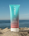 COOLA Hydrating Sunscreen Lotion Guava Mango SPF 50 sitting in sand with scenic ocean background