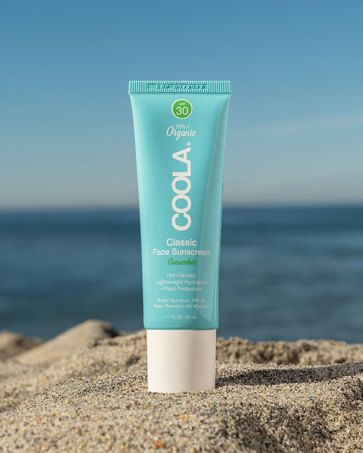 COOLA Classic Face Sunscreen Lotion Cucumber SPF 30 sitting in sand with scenic ocean background