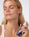 Woman applying COOLA Refreshing Water Mist to face against white background