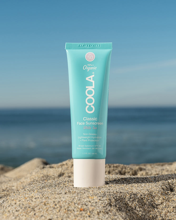COOLA Classic Face Sunscreen Lotion White Tea SPF 50 sitting in sand with scenic ocean background