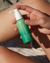Person holding COOLA Scalp & Hair Mist Sunscreen SPF 30 at the beach