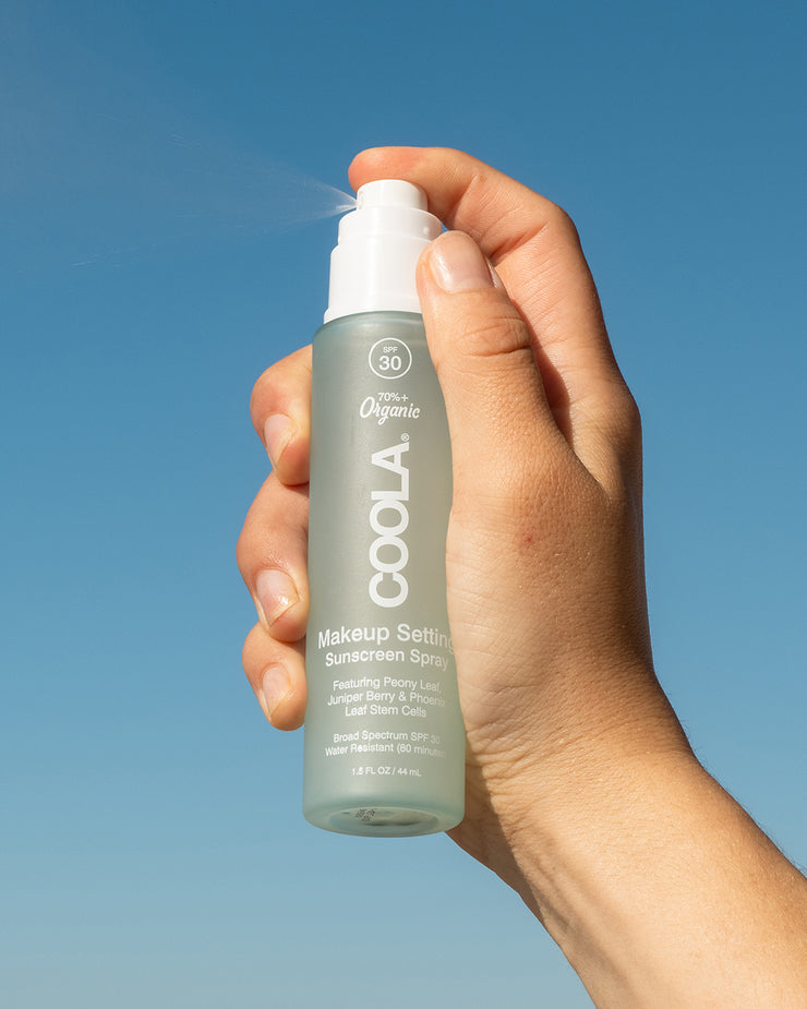 COOLA Makeup Setting Spray being sprayed in air with sky in background