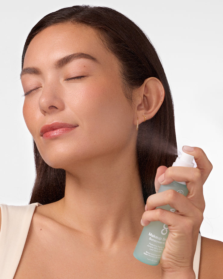 Woman spraying COOLA Makeup Setting Spray to face with white background