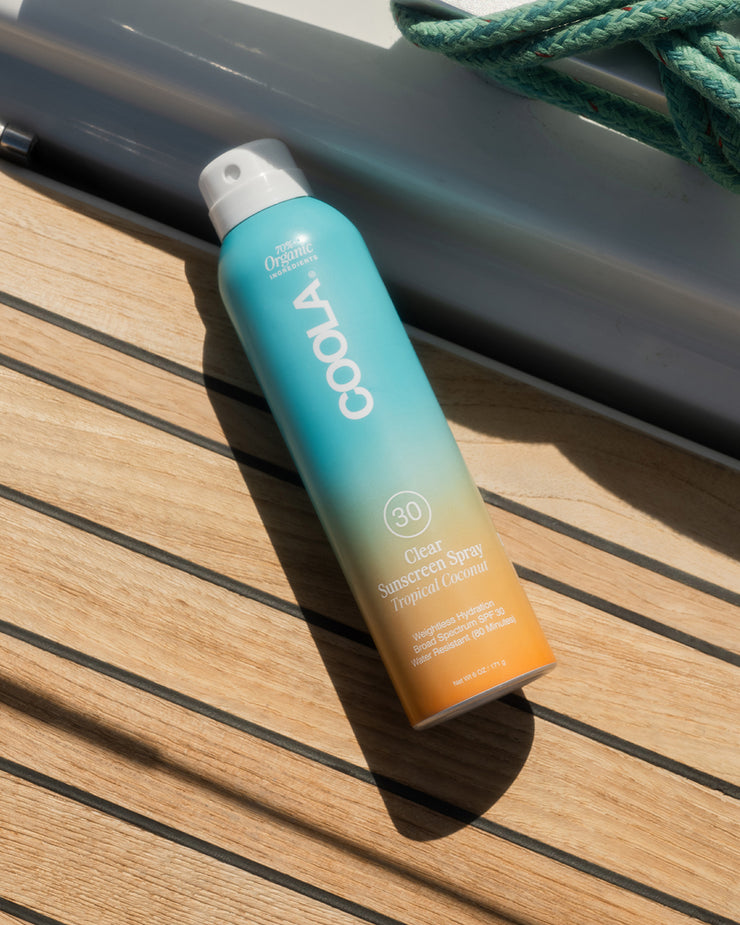 COOLA Clear Sunscreen Spray Tropical Coconut SPF 30 laying on wooden boat deck