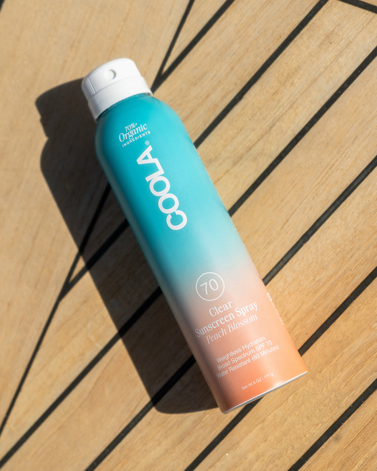COOLA Clear Sunscreen Spray Peach Blossom SPF 70 laying down on wooden deck