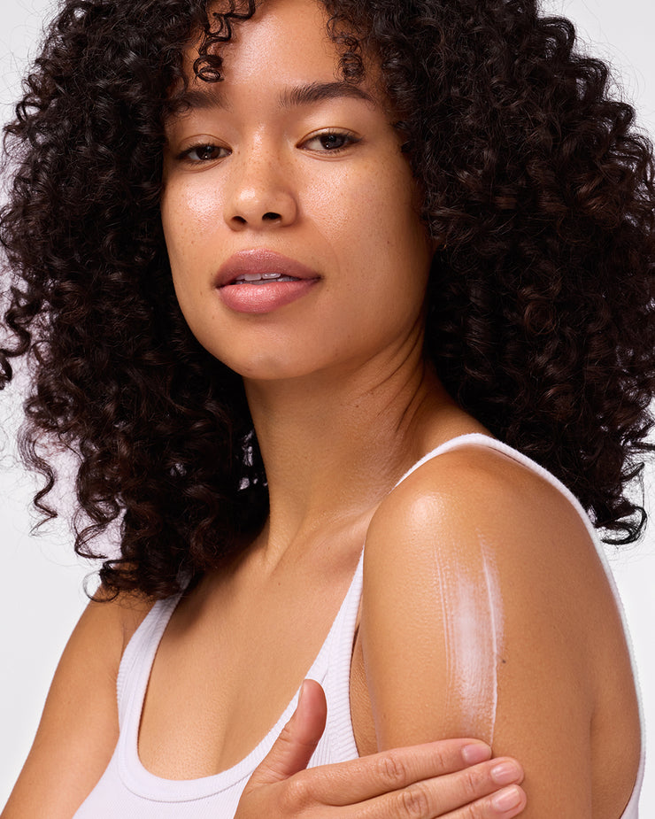 Woman applying COOLA Radical Recovery Moisturizing Lotion to upper arm with white background
