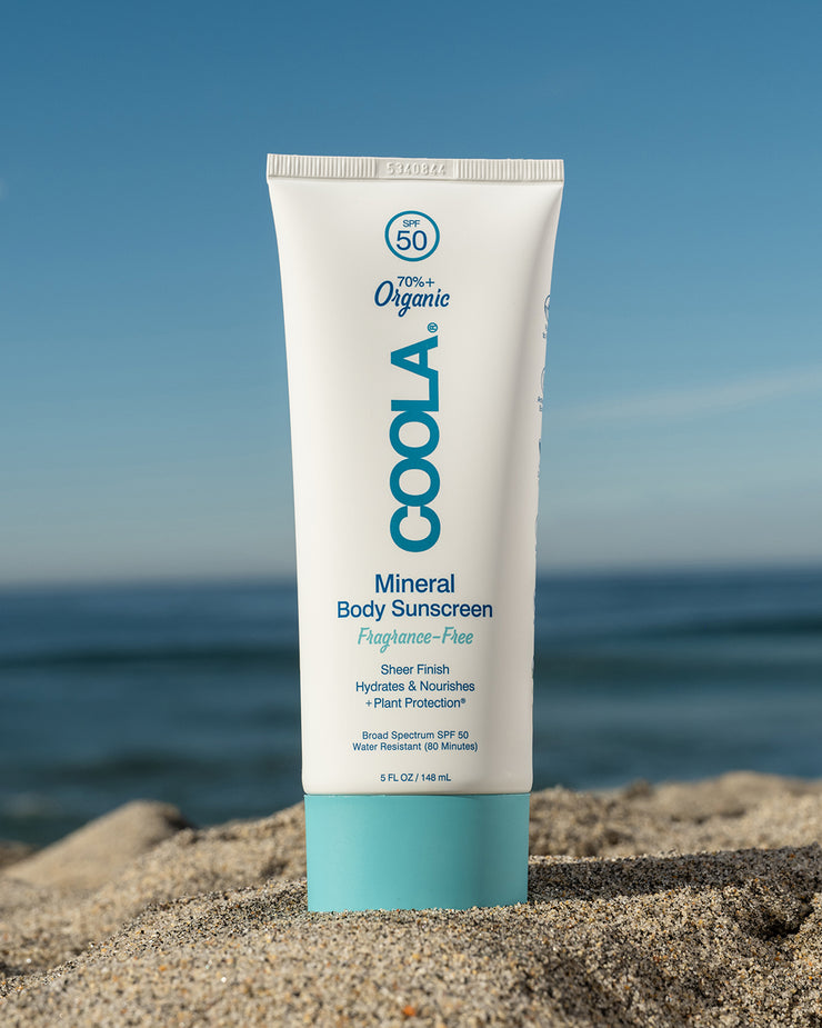 COOLA Mineral Body Sunscreen Lotion Fragrance Free SPF 50 sitting in sand with scenic ocean background