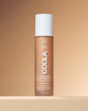 Coola Rosilliance Tinted Moisturizer bottle on a beige background