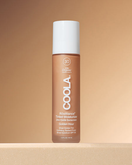 Coola Rosilliance Tinted Moisturizer bottle on a beige background