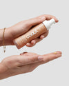 Hand holding Coola tinted moisturizer dispensing into other hand