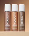 Three bottles of Coola tinted moisturizer on a brown background