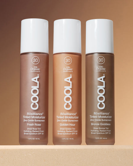 Three bottles of Coola tinted moisturizer on a brown background