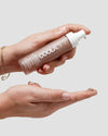 Hand holding a COOLA sunscreen bottle against a neutral background