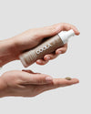 Hand holding Coola Rosilliance Bronze Goddess Tinted Moisturizer dispensing into other hand with a neutral background
