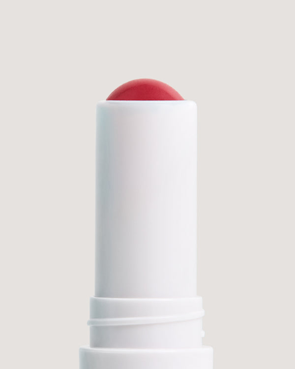 Close-up of white stick showing formula for COOLA Firecracker Mineral Liplux against a beige background.