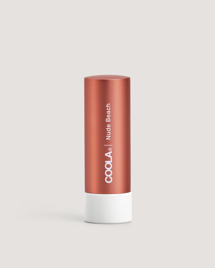 A stick of COOLA Liplux Tinted Lip Balm in a nude beach shade, with a copper-colored body and white base.
