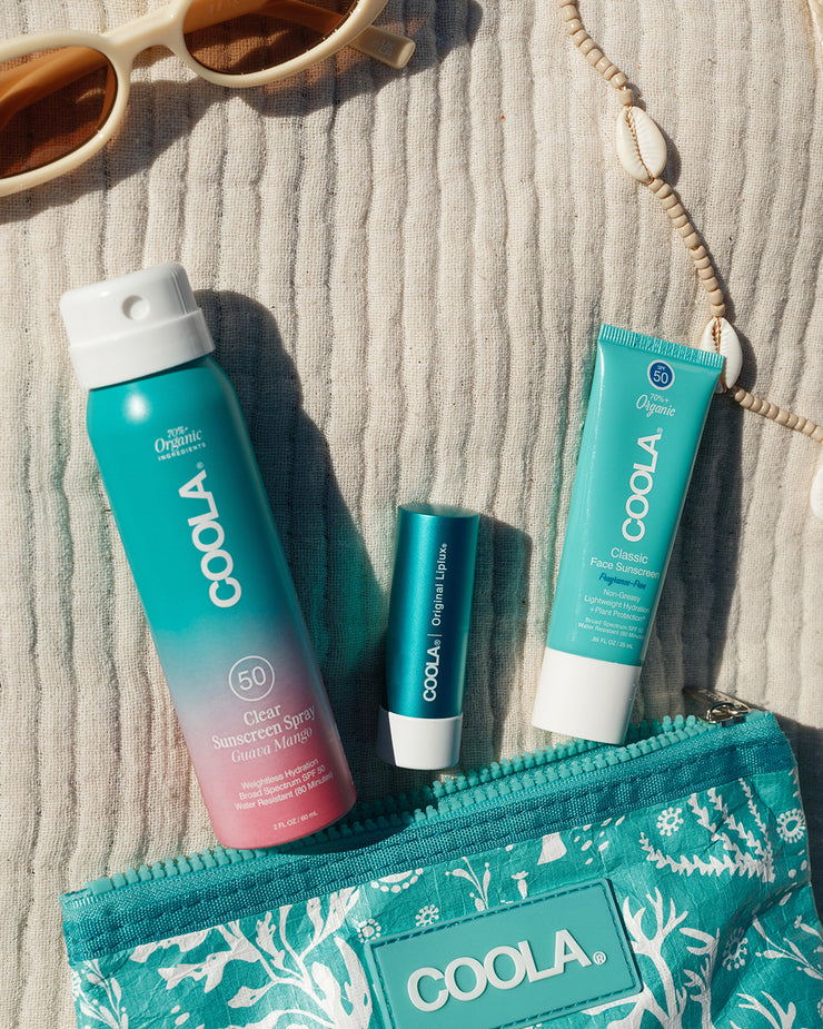 COOLA three piece travel kit with Guava Mango spray, Classic Liplux, and Classic Face Lotion Fragrance-Free on towel.