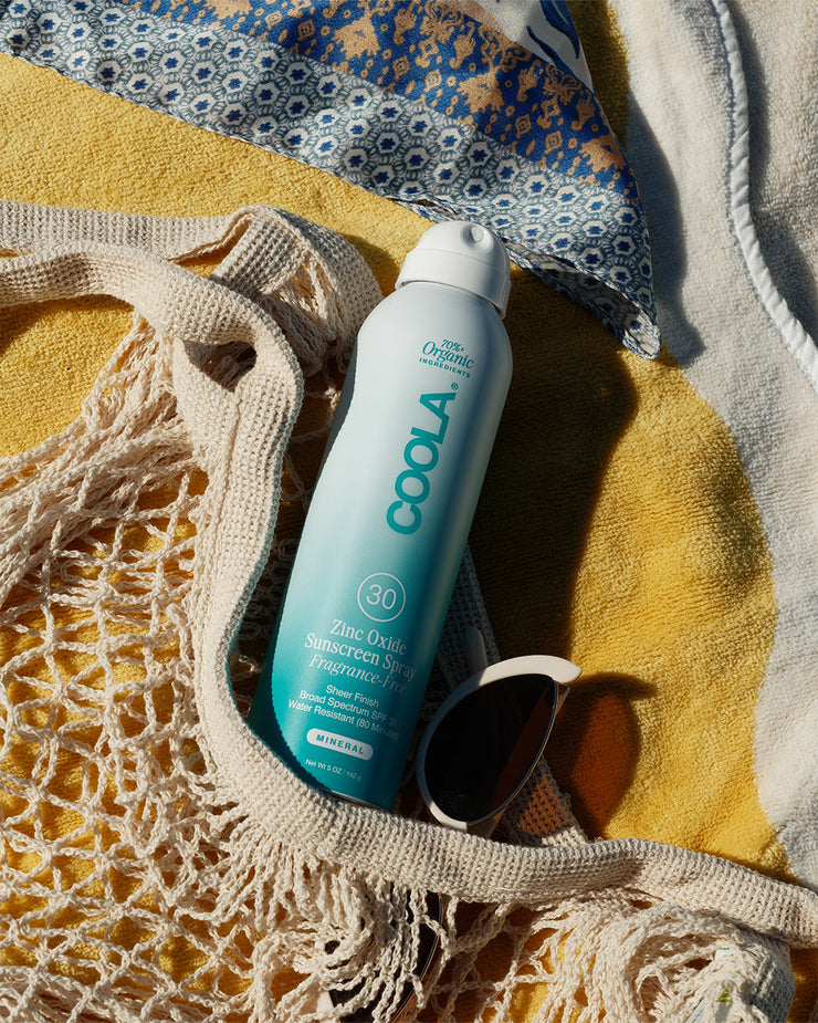 COOLA Zinc Oxide Sunscreen Spray laying in beach bag on yellow towel