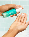 Person holding COOLA Vital Rush Skin Renewal Serum applying to hand in bathroom.