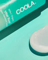 Close-up on COOLA Vital Rush Skin Renewal Serum with formula on teal background.