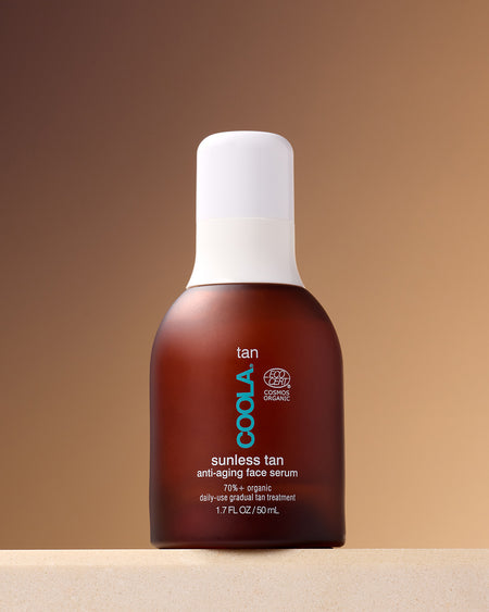 COOLA Sunless Tan Anti-Aging Face Serum standing on counter against tan background.