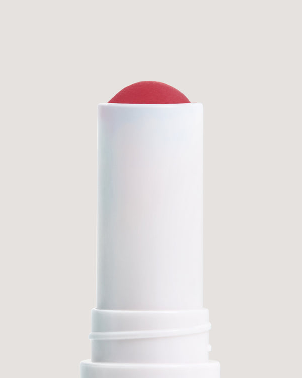 A stick of COOLA Tinted Liplux uncapped showing red tinted formula