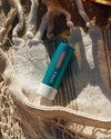 Stick of COOLA Tinted Liplux laying on beach towel