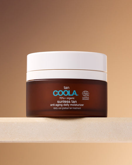 COOLA Sunless Tan Anti-Aging Daily Moisturizer in brown jar siting on shelf against tan background.