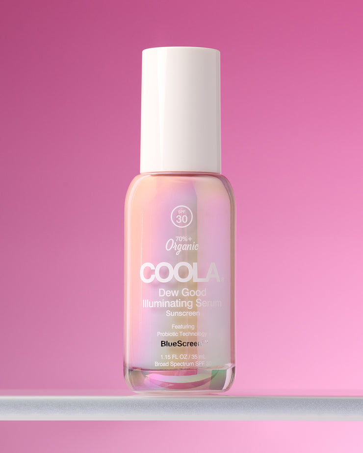 COOLA Dew Good Illuminating Serum SPF 30 sitting on glass shelf against pink background