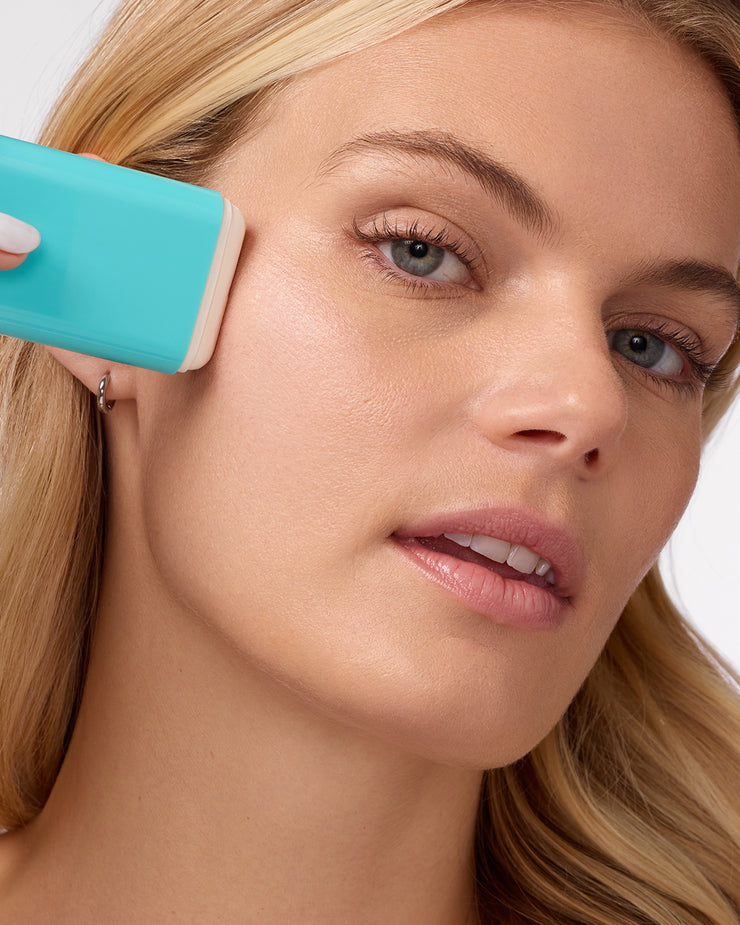 Woman applying COOLA Mineral Sunscreen Stick to cheek with white background.