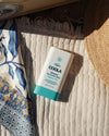 COOLA Mineral Sunscreen Stick Fragrance-Free SPF 50 sitting on towel at the beach.