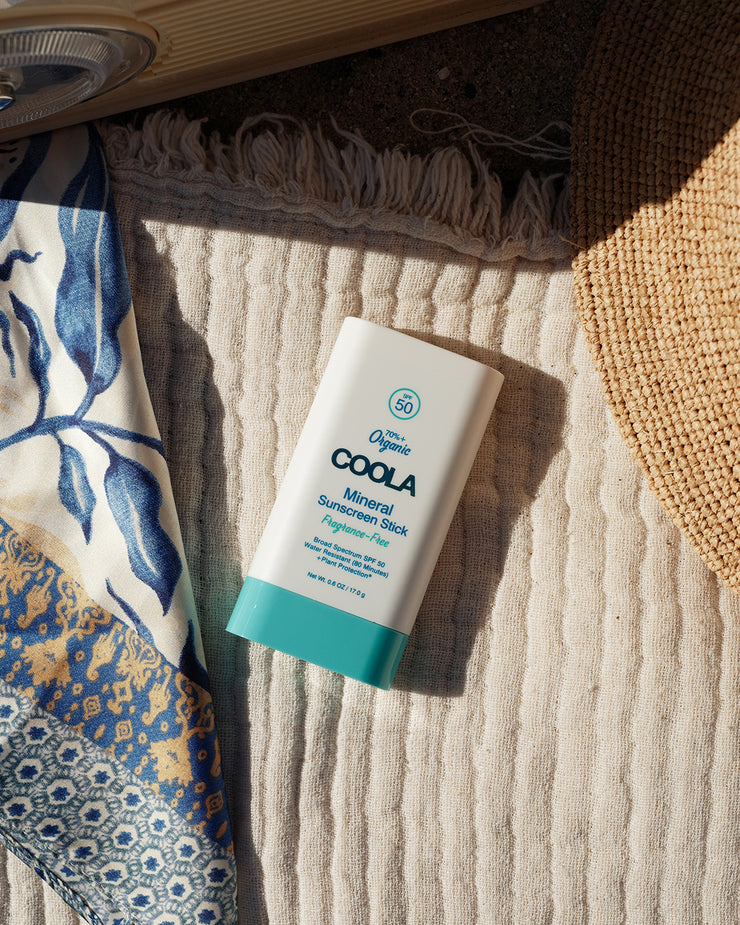 COOLA Mineral Sunscreen Stick Fragrance-Free SPF 50 sitting on towel at the beach.