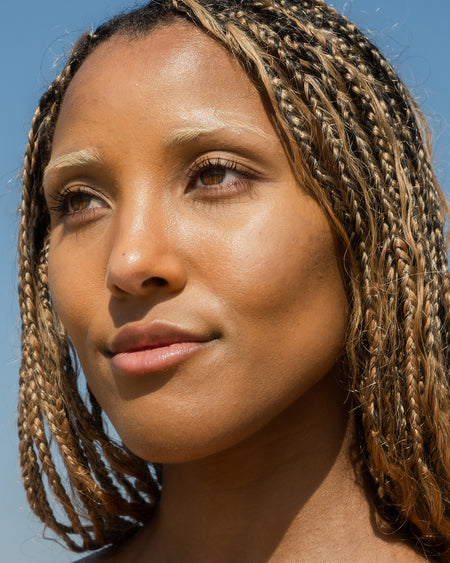 Close-up of woman's face with moisturized skin and blue sky background.