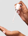 Hand dispensing COOLA Sun Silk Drops Sunscreen SPF 30 in other hand against white background
