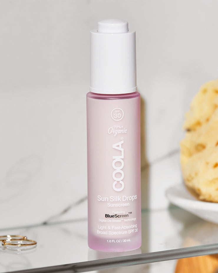 COOLA Sun Silk Drops Sunscreen SPF 30 sitting on glass shelf in bathroom