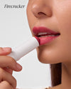 Close-up of woman applying COOLA Mineral Tinted Liplux Firecracker against white background.