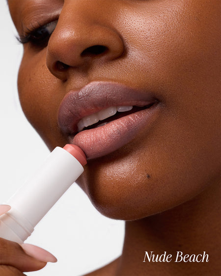 Close-up of woman applying COOLA Mineral Tinted Liplux Nude Beach against a white background.