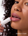 Close-up of woman applying COOLA Mineral Tinted Liplux Summer Crush against white background.