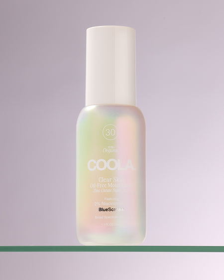 Bottle of COOLA Clear Skin Oil-Free Moisturizer Zinc Oxide Sunscreen sitting on glass shelf with white background