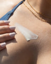 Close-up of woman applying COOLA Dew Good Illuminating Body Melt Lotion SPF 40 formula to chest