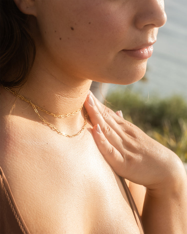 Woman applying COOLA Dew Good Illuminating Body Melt Lotion SPF 40 with scenic coastal background
