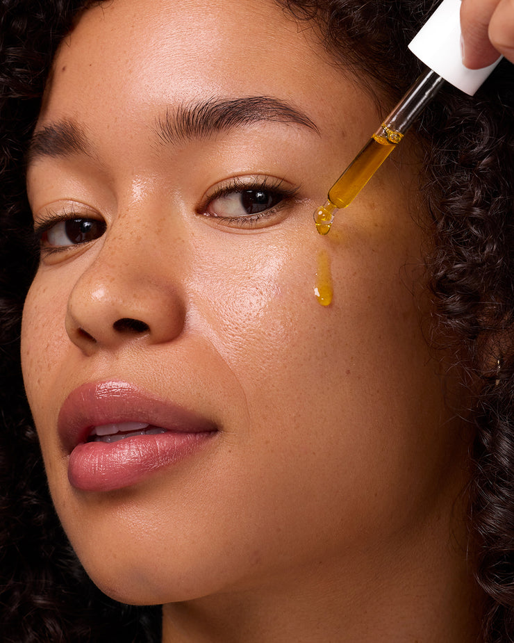 Woman applying COOLA Firming Face Oil to cheek