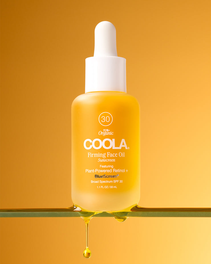 COOLA Firming Face Oil sitting on glass shelf against yellow background