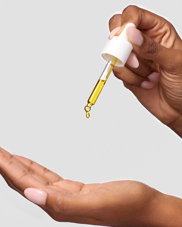 Woman dispensing COOLA Firming Face Oil into hand against white background