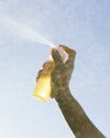 Person spraying COOLA Body Oil Mist with sky background
