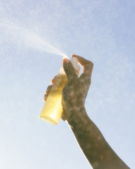 Person spraying COOLA Body Oil Mist with sky background