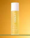 COOLA Body Oil Mist sitting on glass shelf against yellow background
