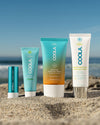 4 travel-sized sunscreen products sitting in sand at beach with scenic ocean view in background
